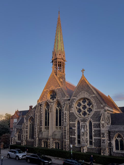 A large, historic church building with intricate Gothic Revival architectural details, including arched windows with stained glass, and a central circular window with tracery. The facade features red