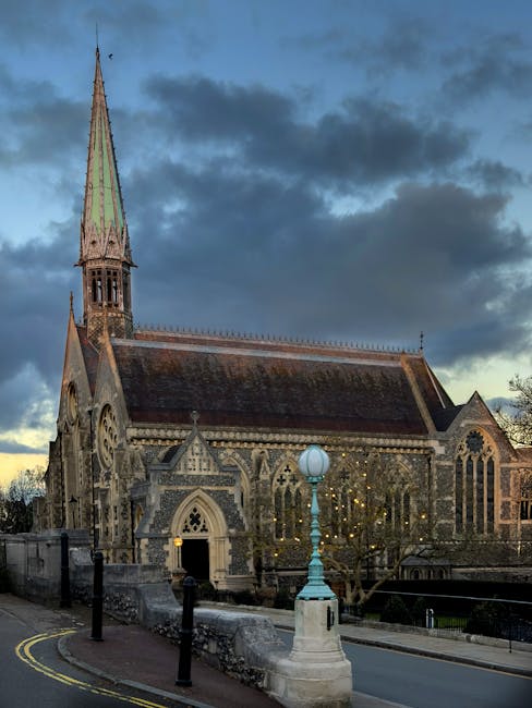 A traditional brick church building with a steeply pitched roof, featuring Gothic-style arched windows with intricate tracery, a circular rose window, and a central arched entrance. The church is surr